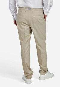 Beige op maat gemaakte broek met een gladde textuur, twee achterzakken en een slim fit, gecombineerd met witte sneakers.