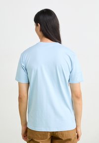 Light blue cotton t-shirt with short sleeves and a round neck. Smooth texture, casual fit. Worn with khaki-colored pants.