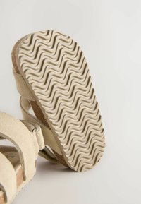 Beige Wildledersandale mit einer strukturierten, gewellten Gummisohle. Verfügt über zwei Riemen und ein glattes Fußbett, das für Komfort und Unterstützung ausgelegt ist.