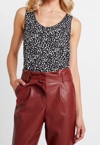 Tílko s potiskem zvířecí kůže v černé a bílé barvě; ve spojení s kalhotami s vysokým pasem z umělé kůže v barvě burgundského vína, které mají přední zavazování a sklady.