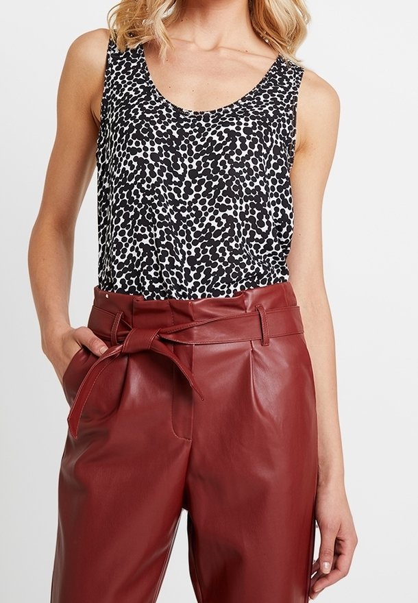 Tílko s potiskem zvířecí kůže v černé a bílé barvě; ve spojení s kalhotami s vysokým pasem z umělé kůže v barvě burgundského vína, které mají přední zavazování a sklady.