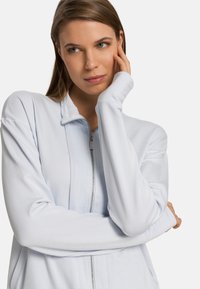 Jasnoniebieska kurtka zapinana na zamek, wykonana z miękkiego materiału, z wysokim kołnierzem i długimi rękawami, ozdobiona srebrnym zamkiem i subtelną teksturą.