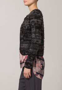 Cárdigan negro texturizado con un acabado suave y bordes lisos en contraste, superpuesto a una blusa de múltiples patrones en rosa y gris.