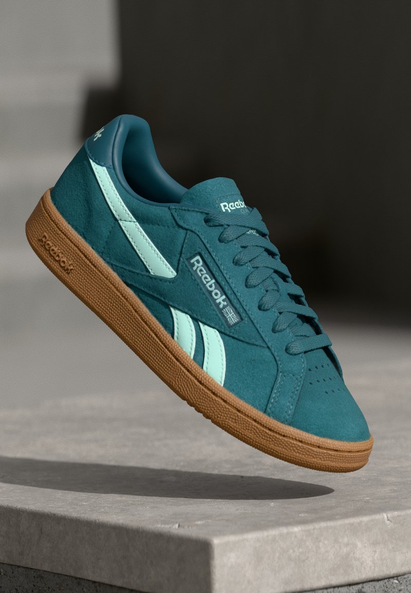 Teal semišové tenisky s mátovými akcenty a světle modrými pruhy, s texturovanou gumovou podrážkou a klasickým brandingem Reebok.