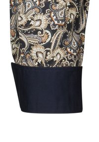 Polsino di una camicia a maniche lunghe con un intricato motivo paisley in nuance di oro, marrone e crema su uno sfondo nero; tessuto blu al bordino del polsino.