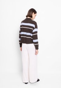 Brązowy i jasnoniebieski sweter w paski o luźnym kroju, z długimi rękawami i kołnierzykiem, zestawiony z białymi spodniami o szerokim kroju i wysokim stanem.