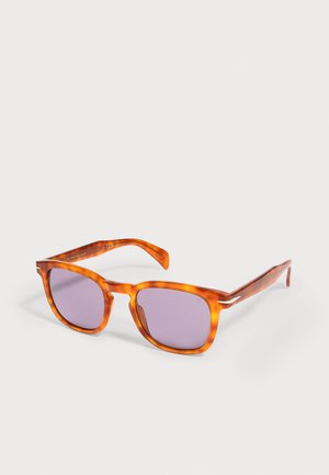 Gafas de sol cuadradas con montura carey y lentes tintadas de color púrpura, reposando sobre una superficie blanca.