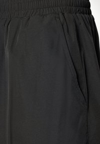 Schwarze, leichte Hose mit einem elastischen Bund, ausgestattet mit Seitentaschen und einer glatten, dezenten Textur. Keine sichtbaren Muster oder Hardware.