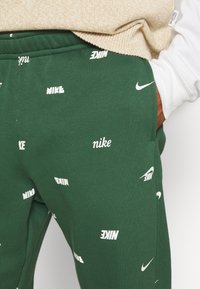 Gröna sweatpants med vita Nike-logotyper överallt. Tillverkade av mjuk bomull, med elastisk midja och sidofickor. Avslappnad design.