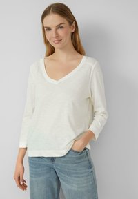 Witte lange mouwen V-hals top met een ontspannen pasvorm, zachte textuur en subtiel gemêleerd patroon, in combinatie met lichtblauwe denim jeans.