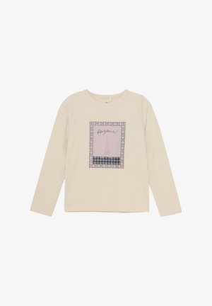 Cremefarvet langærmet skjorte med et grafisk design af Eiffeltårnet og ordet "bonjour!" mod en pink og mønstret baggrund.