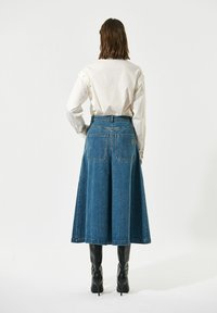 Denimska krila s razširjeno obliko, modre barve in zadnjimi žepi. V kombinaciji z belo srajco, oblečena z črnimi visokimi petami.