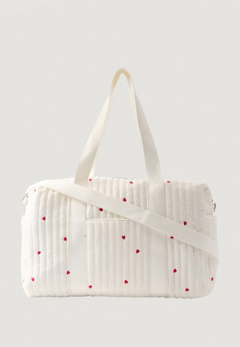 Λευκή καπιτονέ τσάντα duffel με μικρά κόκκινα μοτίβα σε σχήμα καρδιάς, με δύο κοντά χερούλια και ένα ρυθμιζόμενο λουρί ώμου.