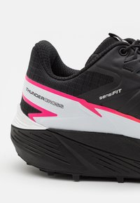 Czarne buty sportowe z różowymi i białymi akcentami. Posiadają teksturowaną cholewkę, wyściełany zapiętek oraz gumową podeszwę z wzorami zapewniającymi przyczepność.