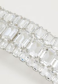 Bracciale in tonalità argento con grandi cristalli trasparenti rettangolari fissati con una montatura a griffe, che presenta una superficie lucida e riflettente.