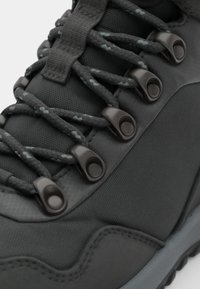 Bota de caminhada preta com um upper texturizado e acabamentos lisos, ilhós reforçados e atacadores estampados para um fecho seguro.
