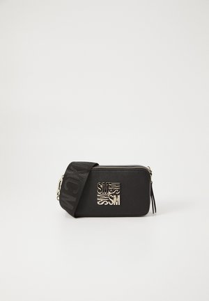 Sac bandoulière rectangulaire noir avec logo métallique SM doré et large sangle noire avec texte en relief sur fond blanc uni.