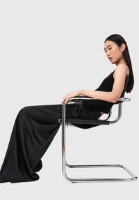 Sort ribbet tanktop kombineret med brede sorte bukser, siddende på en krom cantilever-stol med et minimalistisk design.