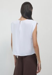 Blusa corta bianca a maniche corte con dettaglio a chiave sul retro, realizzata in un tessuto leggero e liscio. Fit semplice e rilassato senza alcun arredamento.