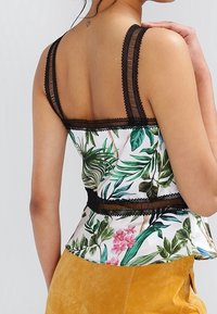 Top senza maniche con stampa floreale su sfondo bianco, foglie di palma verdi e fiori rosa. Bordo in pizzo nero e spalline regolabili.