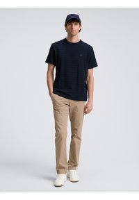Camiseta de rayas marinas, de manga corta y cuello redondo; combinada con chinos beige y zapatillas blancas; también incluye una gorra marina.