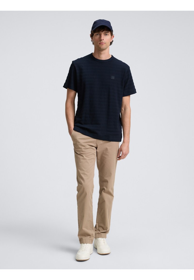Camiseta de rayas marinas, de manga corta y cuello redondo; combinada con chinos beige y zapatillas blancas; también incluye una gorra marina.