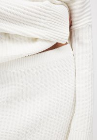 Gestreifter weißer Strick-Co-Ord-Set mit einem taillierten Oberteil mit breitem Saum und einem passenden hochgeschnittenen Rock mit elastischem Bund.