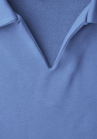 Primo piano di una camicia con colletto azzurro cielo che mostra la trama a maglia all'interno del colletto e il tessuto liscio all'esterno, evidenziando i dettagli e la struttura del tessuto.