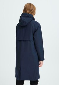 Mornarško modra, plašč do kolen s kapuco, z zadnjim razpiralom, dolgimi rokavi in minimalističnim dizajnom; izdelan iz vodoodpornega materiala.