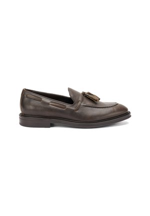 Mocasin de cuero marrón con punta redonda, borlas decorativas, costuras en contraste y una suela de bajo perfil. Textura suave con un acabado pulido.