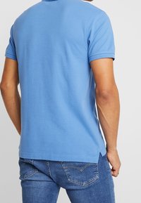 Polo bleu clair avec col classique et manches courtes, en coton, avec fentes latérales à l'ourlet et texture douce.