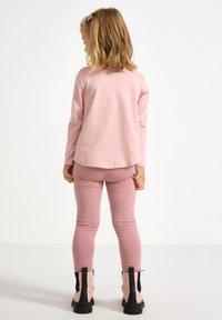 Pink long-sleeve top with a rounded hem, paired with pink leggings. Black and pink ankle boots with zippers and textured soles.