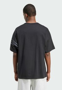 Black oversized t-shirt with a round neckline and short sleeves. Features three dark gray stripes on the left shoulder. Soft, smooth fabric.