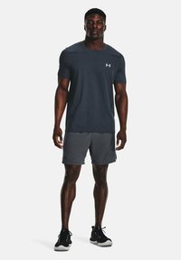 Camiseta atlética de manga corta gris oscuro con un patrón de cuadrícula, combinada con pantalones cortos atléticos grises. Zapatillas negras completan el look deportivo.