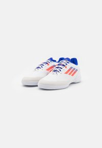 Zapatillas deportivas blancas con diseño texturizado, que presentan acentos en azul y naranja, punta redonda y cierre de cordones. Material sintético ligero.