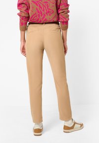 Pantalon kaki à jambe droite, tissu texturé et poches arrière. Associé à des baskets de couleur claire et un pull à motif rose.