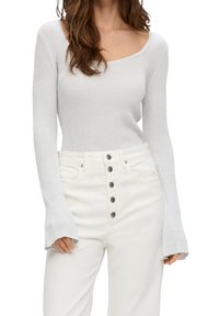 Maglione grigio chiaro a coste con scollo ampio e maniche lunghe, abbinato a pantaloni bianchi a vita alta con fronte a sei bottoni.