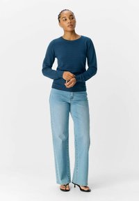 Haut en tricot à manches longues bleu marine avec un col rond. Associé à un jean droit bleu clair et des sandales à talons noires.