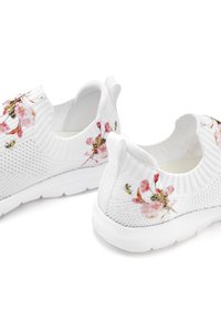 White knit sneakers featuring pink floral embroidery, a flexible slip-on design, and a textured upper with a white rubber sole.