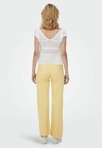 Top de punto blanco con mangas cortas, combinado con pantalones amarillos de campana. El conjunto presenta un corte relajado y un diseño simple.