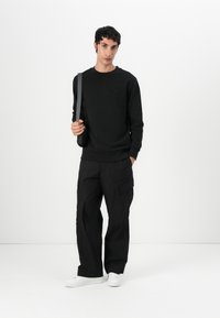 Schwarzer Pullover mit gerippten Bündchen und Rundhalsausschnitt, kombiniert mit schwarzen Cargo-Hosen mit Seitentaschen und weißen Sneakers.