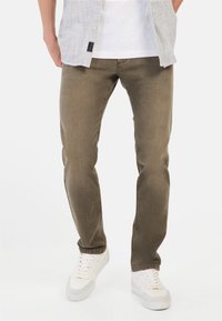Khaki-kleurige jeans met een slim fit en een licht versleten textuur, gecombineerd met witte sneakers en een licht gestreept overhemd met knopen.