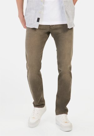 Khaki-kleurige jeans met een slim fit en een licht versleten textuur, gecombineerd met witte sneakers en een licht gestreept overhemd met knopen.