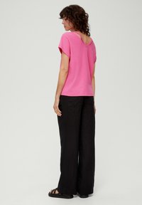 Różowa bluzka z krótkim rękawem i zaokrąglonym dekoltem z tyłu, w zestawie z luźnymi czarnymi spodniami i czarnymi sandałami. Miękki materiał i swobodny krój.