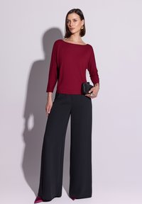 Bordowa bluzka z długim rękawem w połączeniu z czarnymi, szerokimi spodniami oraz małą czarną kopertówką. Gładka tkanina o luźnym kroju.