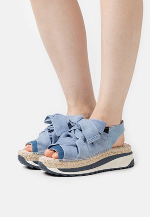 I sandali in tessuto blu presentano grandi fiocchi frontali, un design a punta aperta e una zeppa in juta intrecciata con una robusta suola in gomma.