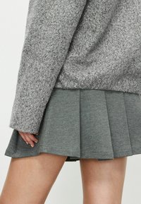 Šedý texturovaný svetr s dlouhými rukávy, který je v kombinaci se šedou skládací sukní, zdůrazňuje měkkou tkaninu s vrstveným designem.