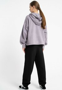 Oversized fioletowa bluza z kapturem i sznurkiem, w połączeniu z luźnymi czarnymi spodniami dresowymi i czarnymi sneakersami.