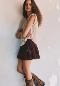 Bordeaux-laagrok met zilveren accenten, gecombineerd met een licht, luchtig beige truitje en hoge bruine suède laarzen.