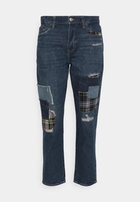 Blå denimjeans med slitna lappar och olika tygdetaljer, inklusive rutigt mönster. Rakt ben-design med standard midjeband.